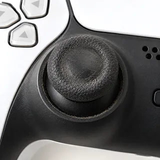 PS5 DualSense controller in white and black, front close-up with a worn left analog stick and grime around its base