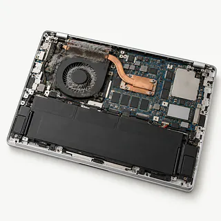 Laptop in silver, bottom cover removed with gray dust clogging the cooling fan and heat sink