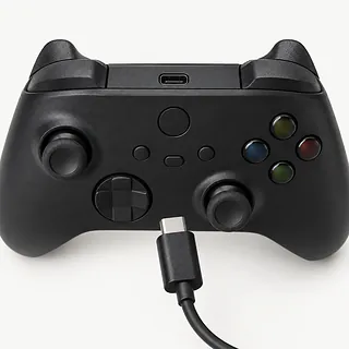 Xbox Wireless Controller in black, face up with gray lint in its charging port and an unplugged cable